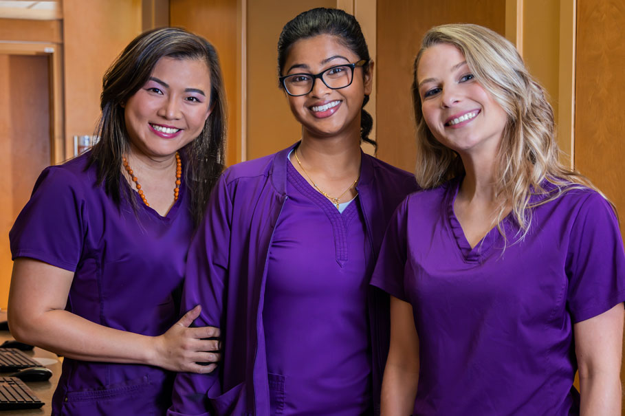 Three nurses in purple scrubs smiling